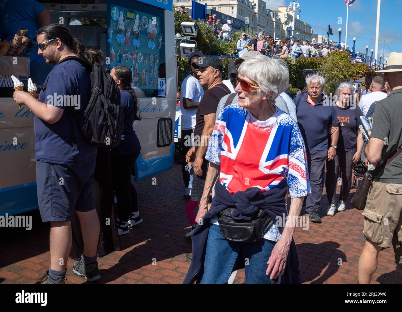Una donna anziana che indossa una T-shirt con bandiera Union Jack cammina tra le folle lungo la passeggiata sul lungomare di Eastbourne mentre assiste all'annuale Eastbourne Air Foto Stock