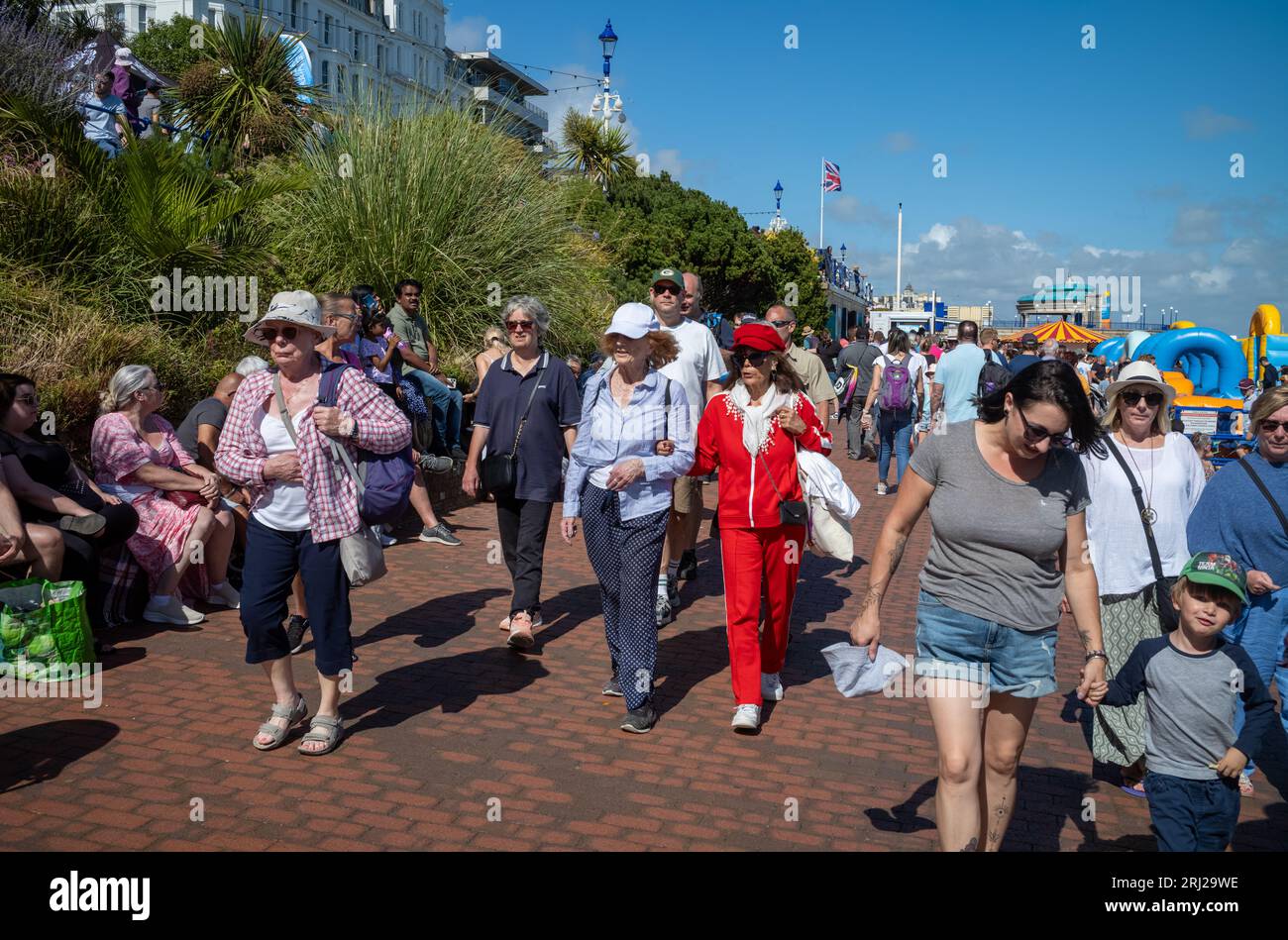 Due eleganti donne anziane camminano a braccetto in folle lungo la passeggiata sul lungomare di Eastbourne mentre assistono all'annuale Eastbourne Airbourne, un inte Foto Stock
