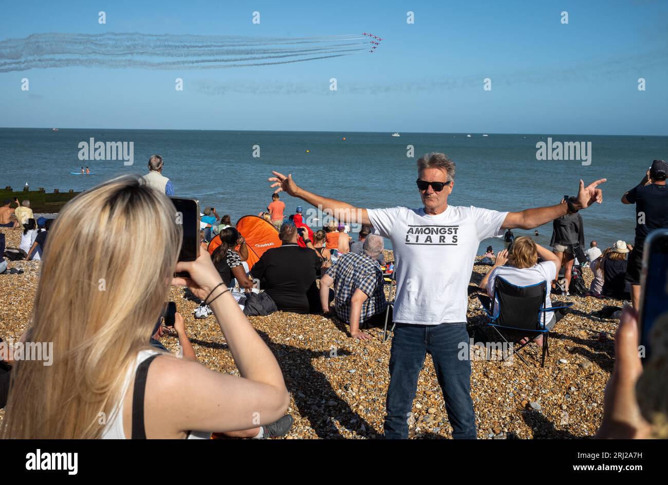 Un uomo che indossa una T-Shirt che pubblicizza la band di Brighton "Amongst Liars" posa per una foto sulla spiaggia di Eastbourne come il famoso team espositivo della RAF, il Red A Foto Stock