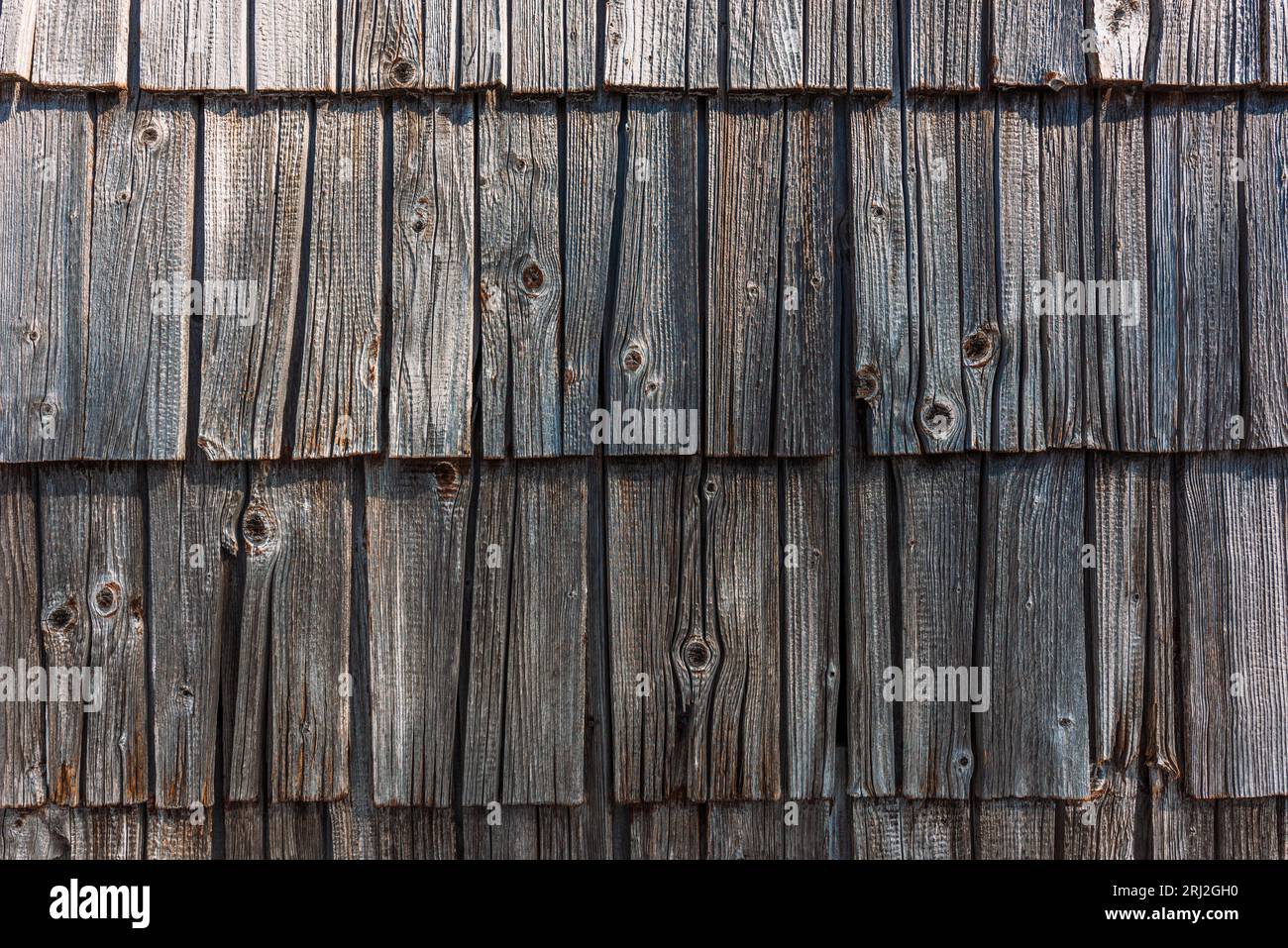 Vecchio cottage di montagna sloveno con facciata in legno piastrellato, piastrelle di legno usurate sul muro esterno come sfondo Foto Stock