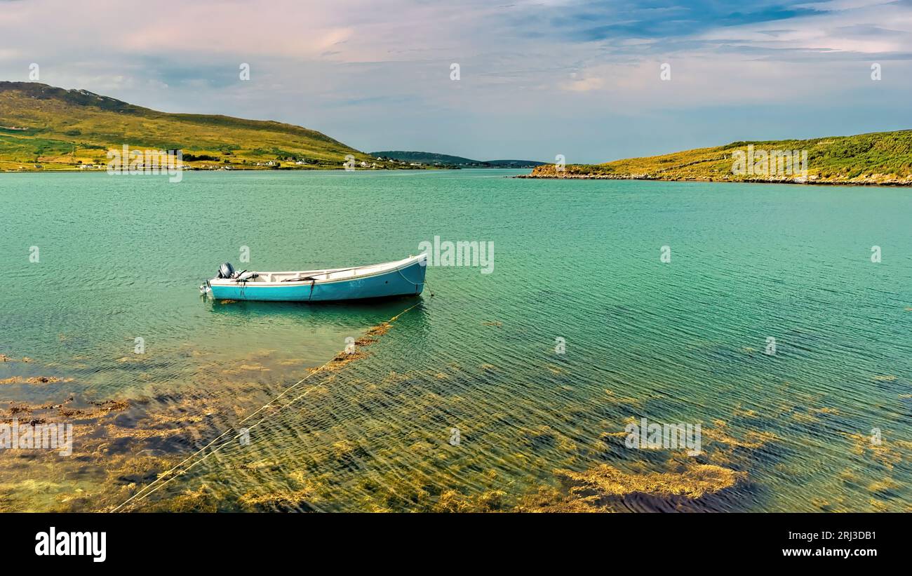 Una barca a vela si vede navigare nel mezzo di un tranquillo specchio d'acqua, circondato da lussureggianti colline verdi e terra sullo sfondo Foto Stock