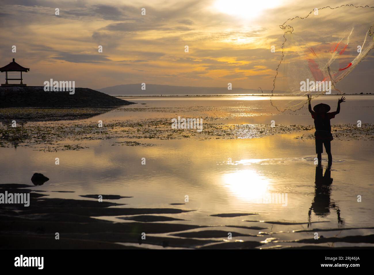 Fisherman indonesiano che lancia una rete con una pagoda sullo sfondo Foto Stock