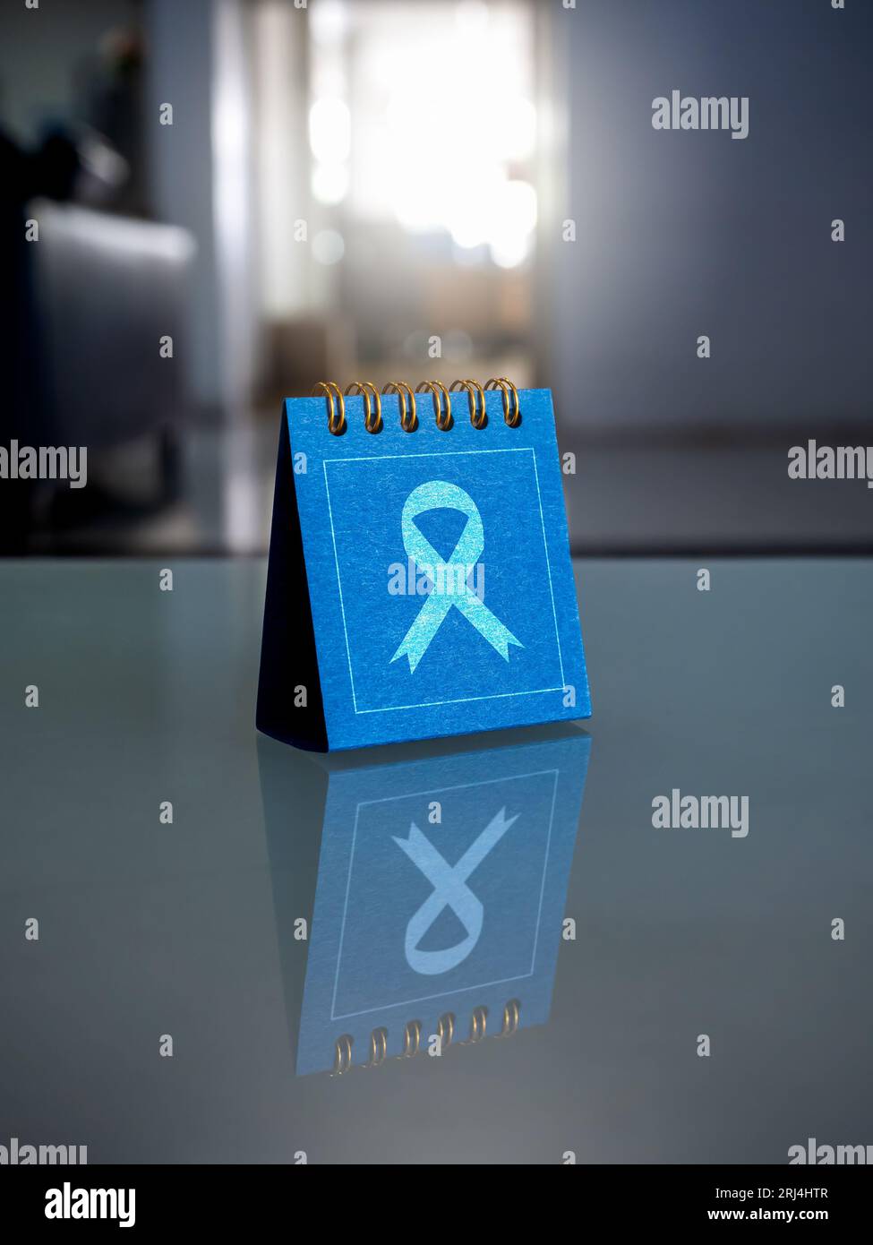 Concetto del giorno del cancro. Icona a nastro sul coperchio blu del calendario della scrivania sul tavolo di vetro. Appuntamento promemoria calendario della campagna per il cancro. Mese di sensibilizzazione al cancro. Foto Stock