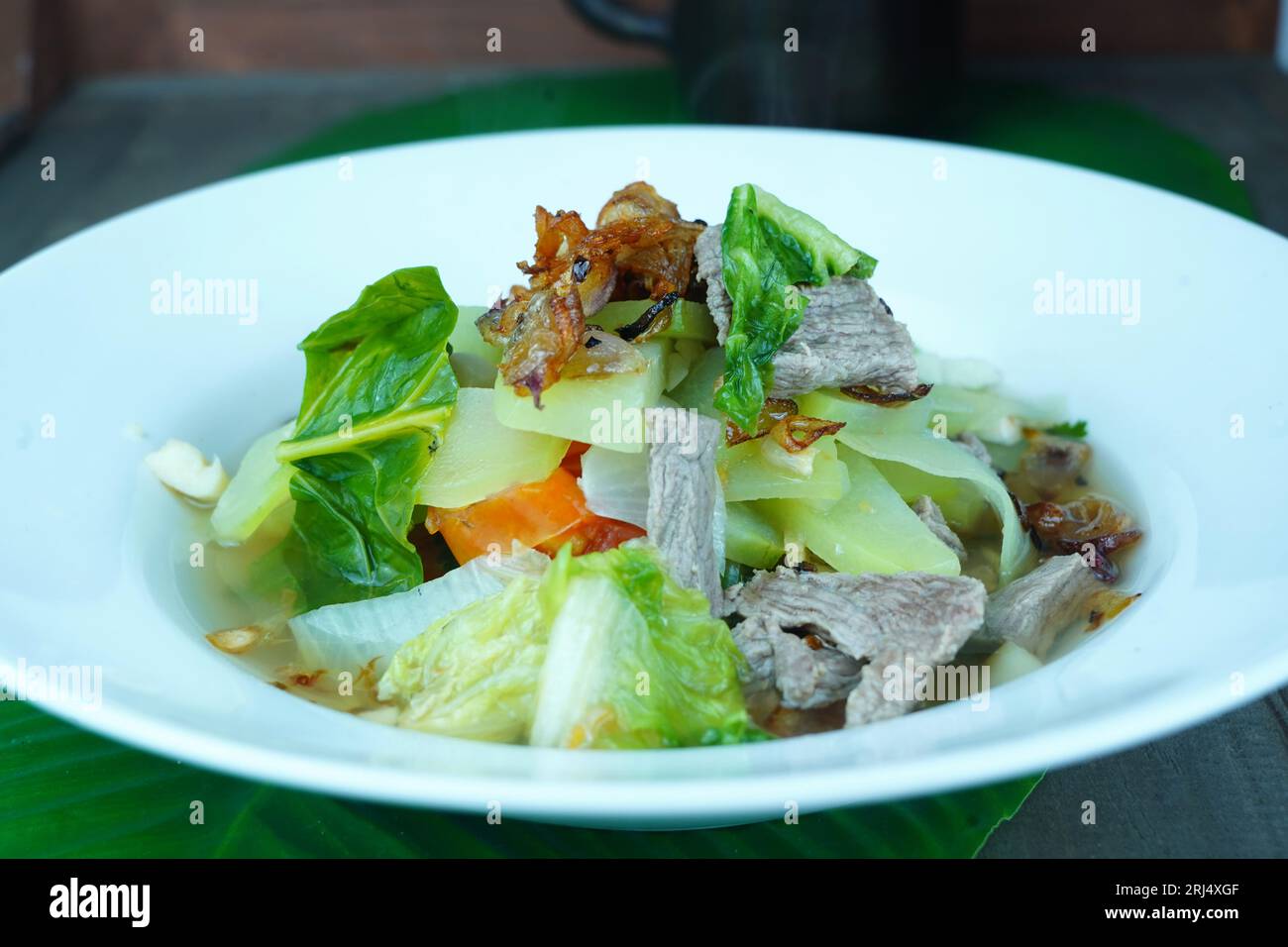 Mescolare il manzo fritto con bok choy e lattuga romaina, servito su un piatto bianco sul tavolo rivestito con foglia di banana. Foto Stock