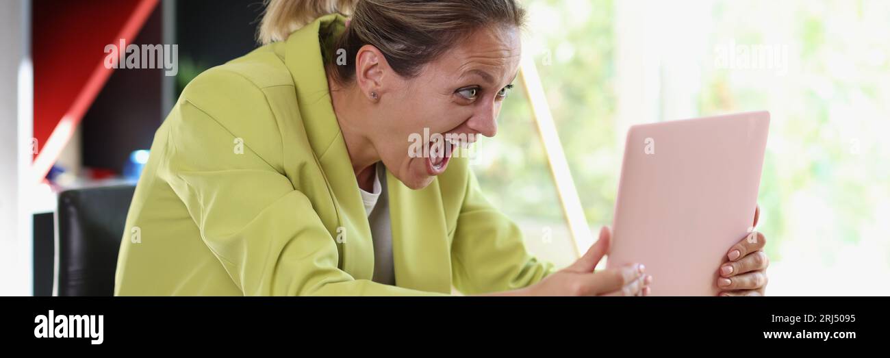 Una donna molto felice tiene il suo notebook in mano sopra il tavolo e guarda lo schermo. Foto Stock