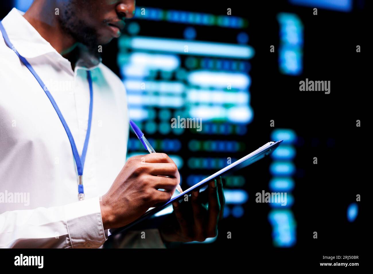 Ingegnere meticoloso che esamina attentamente l'elenco di controllo dettagliato per la manutenzione dei server, monitorando i sistemi critici in strutture high-tech, cercando di identificare e risolvere potenziali malfunzionamenti Foto Stock