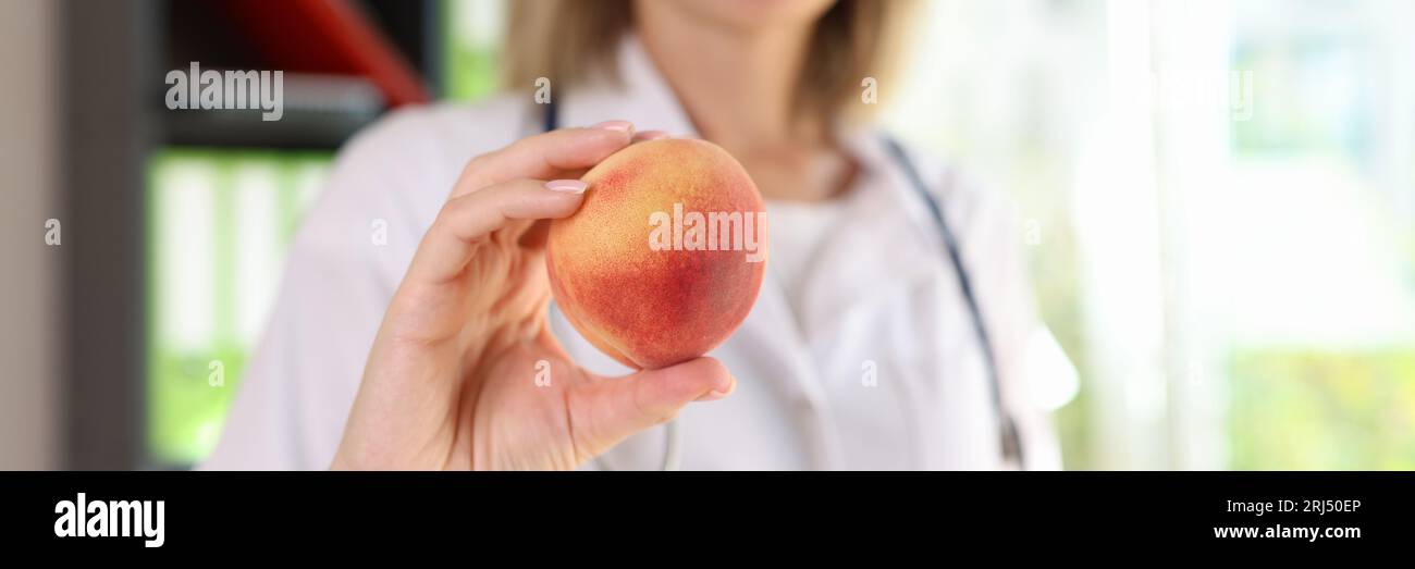 Nutrizionista femminile sorridente tiene in mano frutta fresca di pesca da vicino. Foto Stock