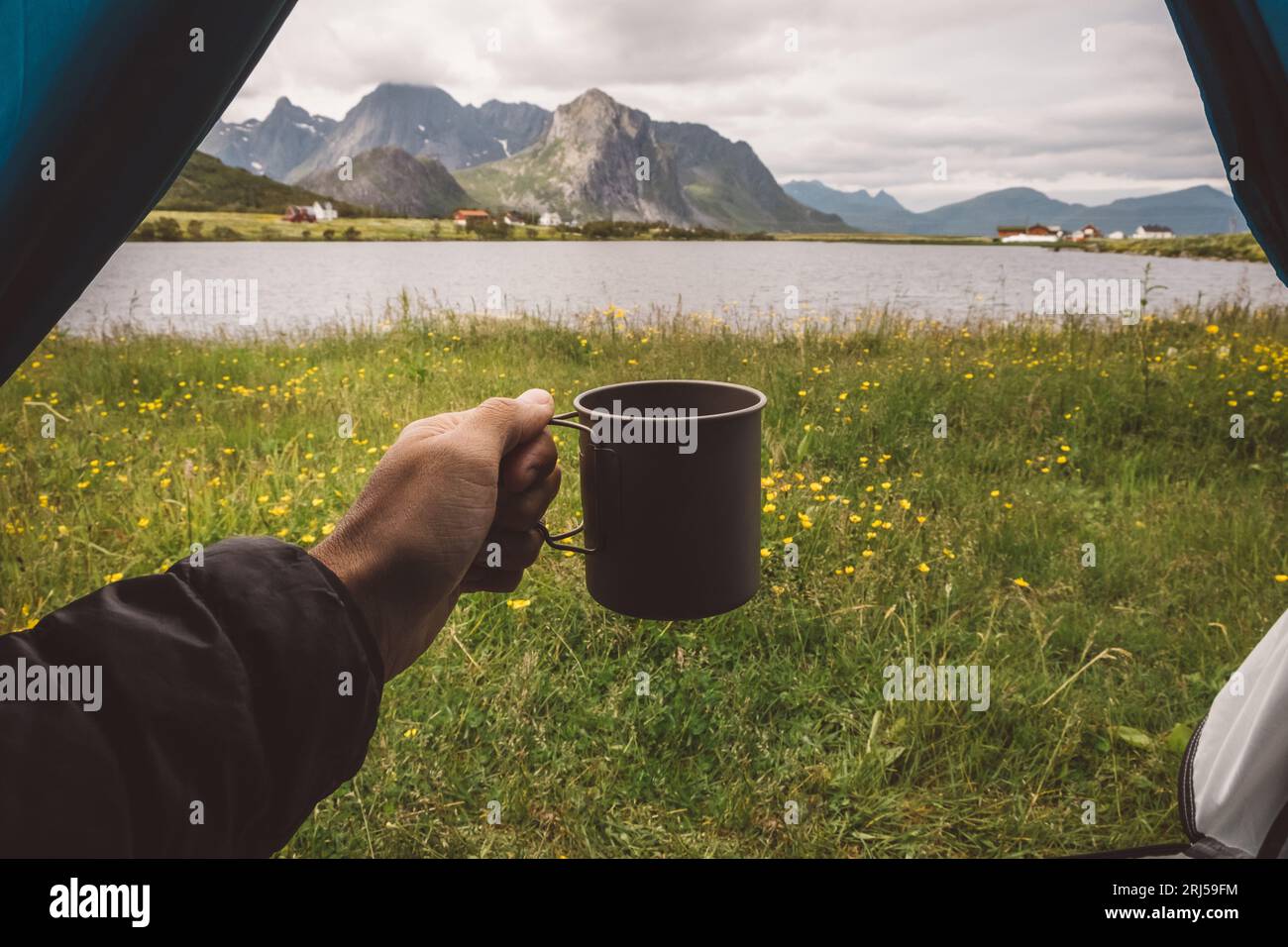 Mano di un uomo che tiene una tazza in una tenda da campeggio con vista lago in Norvegia Foto Stock