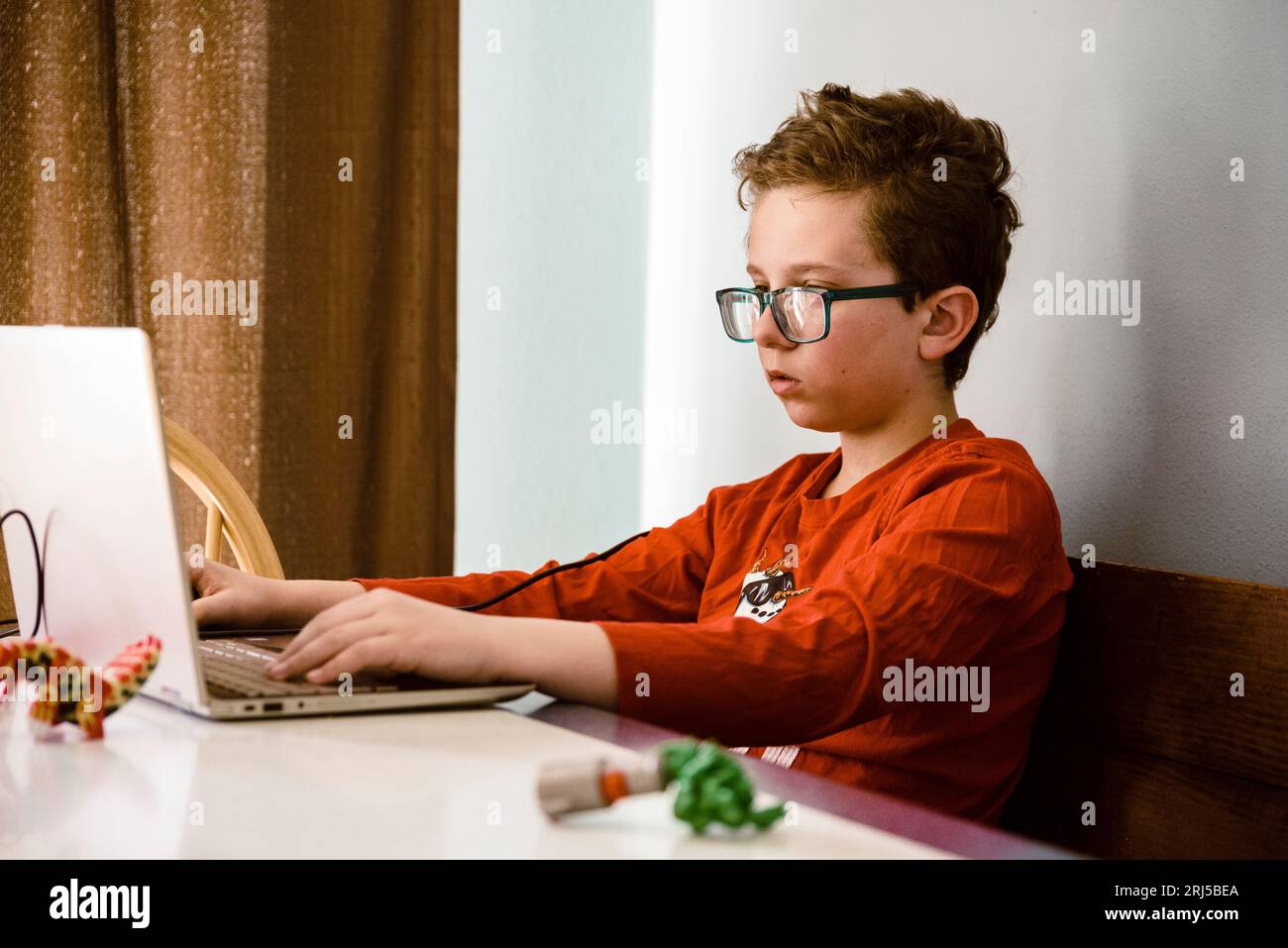 Ragazzo con una camicia rossa che usa un computer al chiuso. Foto Stock