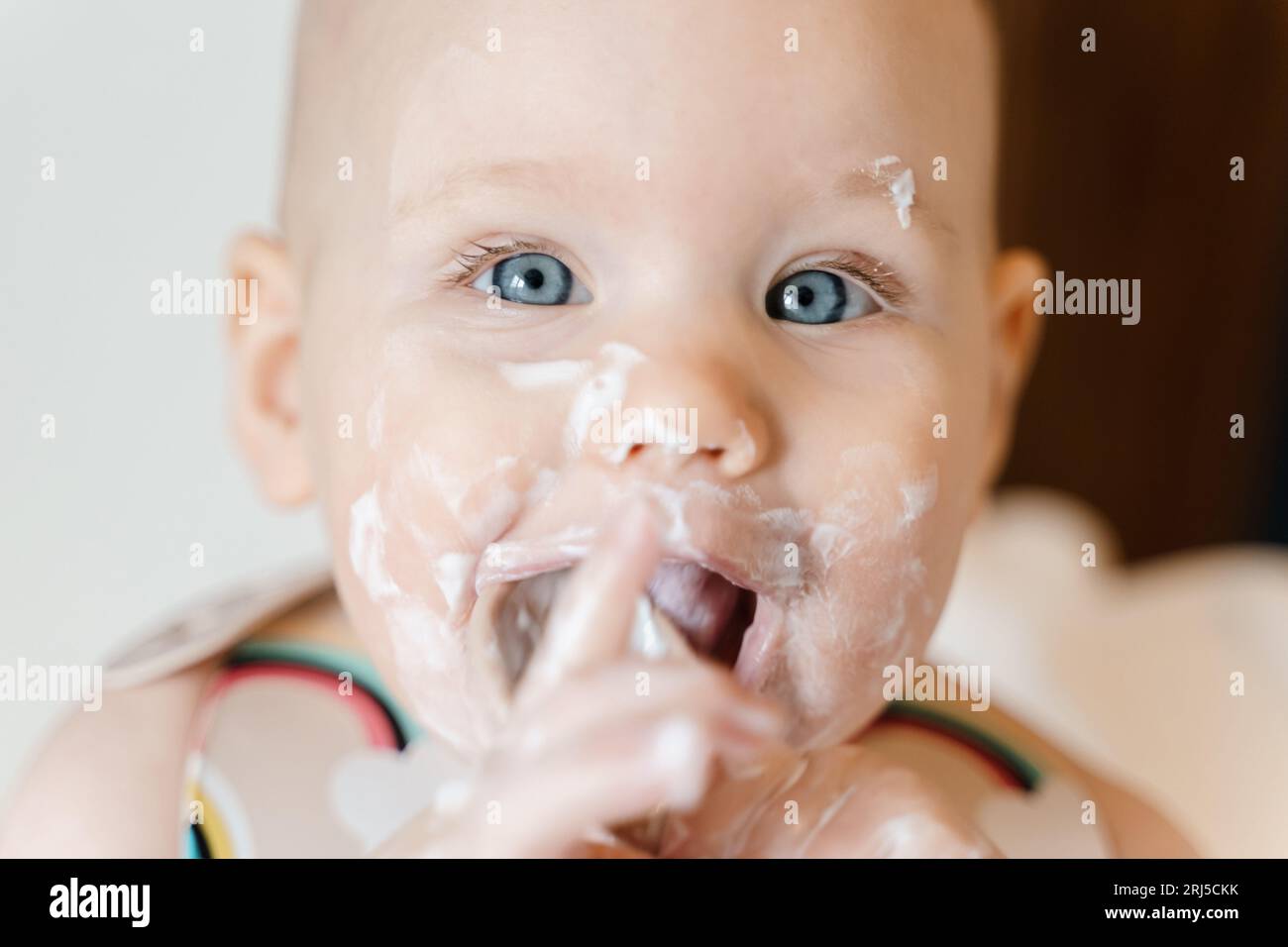 Carino bambino di sei mesi che mangia yogurt da solo Foto Stock
