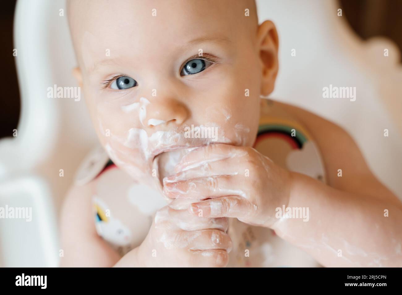 Carino bambino di sei mesi che mangia yogurt da solo Foto Stock