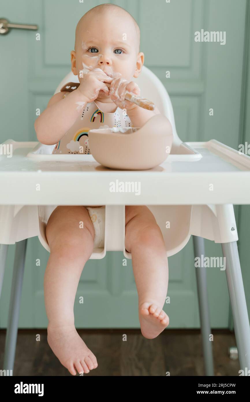 Carino bambino di sei mesi che mangia yogurt da solo Foto Stock
