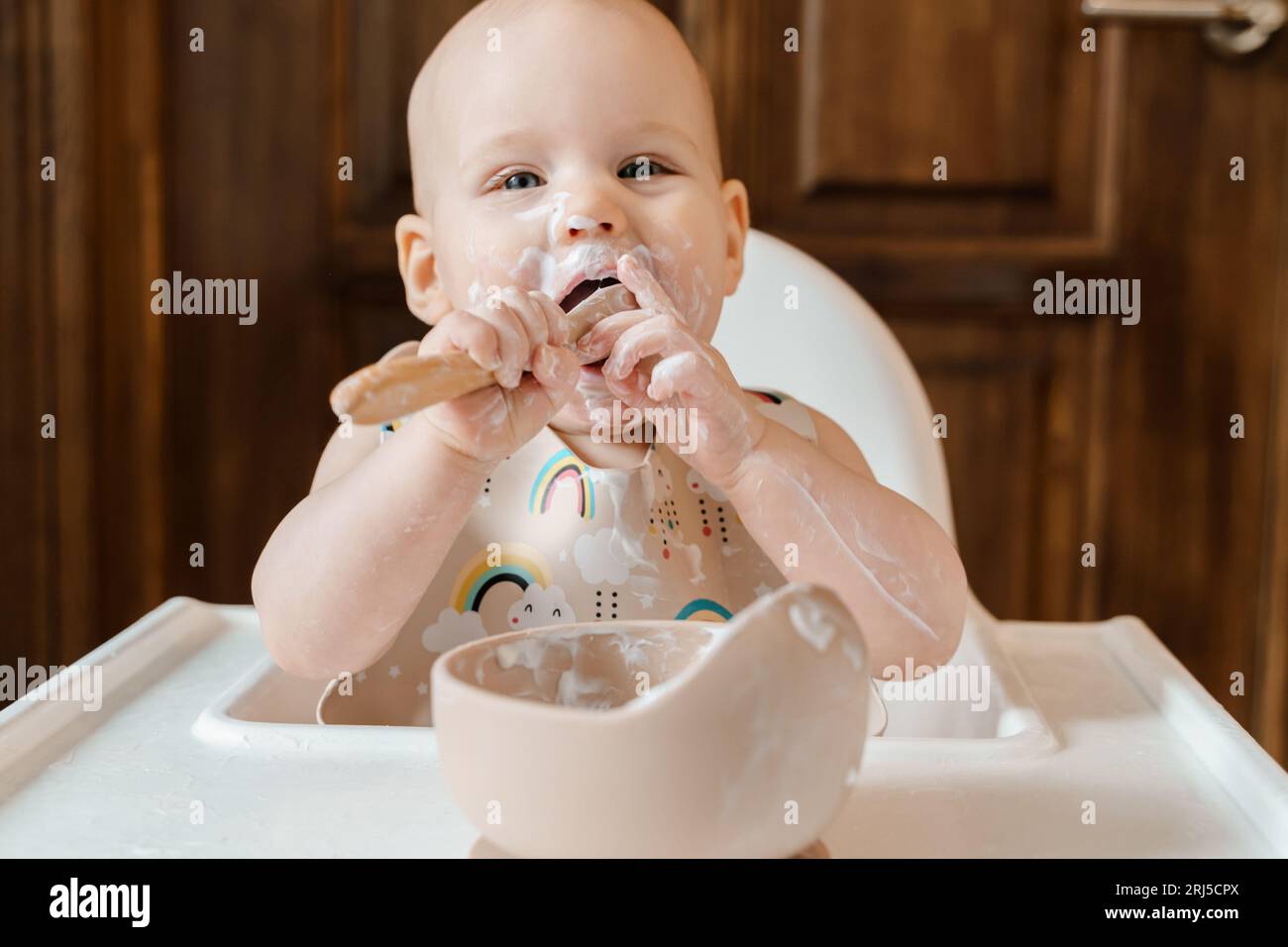 Carino bambino di sei mesi che mangia yogurt da solo Foto Stock