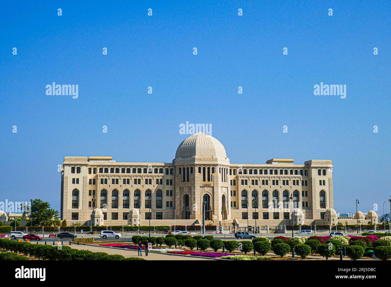 Una vista della Corte Suprema dell'Oman contro un cielo blu brillante e lussureggianti giardini verdi Foto Stock