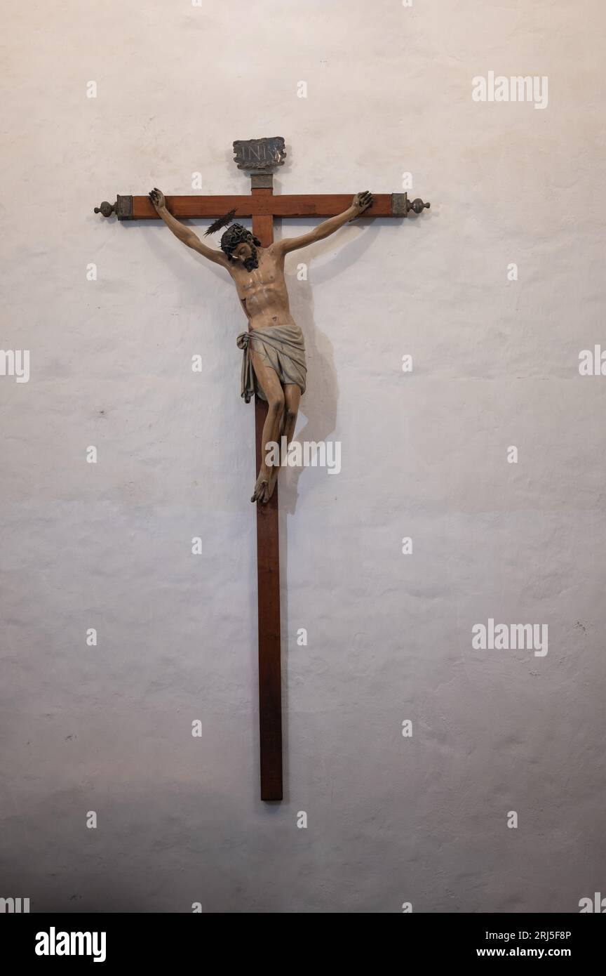 Un primo piano verticale di Gesù Cristo inchiodato alla croce di legno appesa al muro Foto Stock