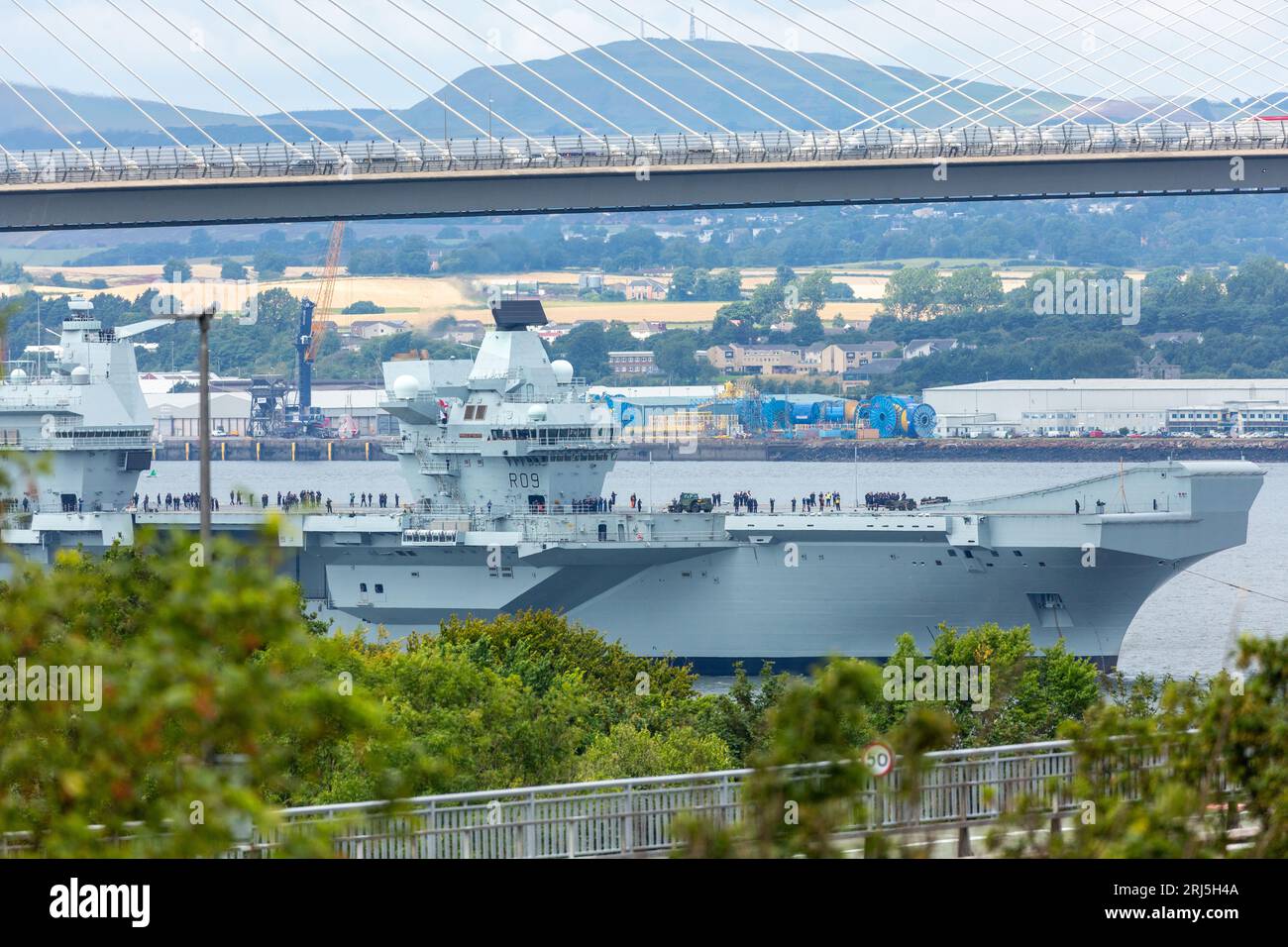 Portaerei HMS Prince of Wales che lascia il porto di Rosyth e naviga sotto il ponte Forth Road Foto Stock