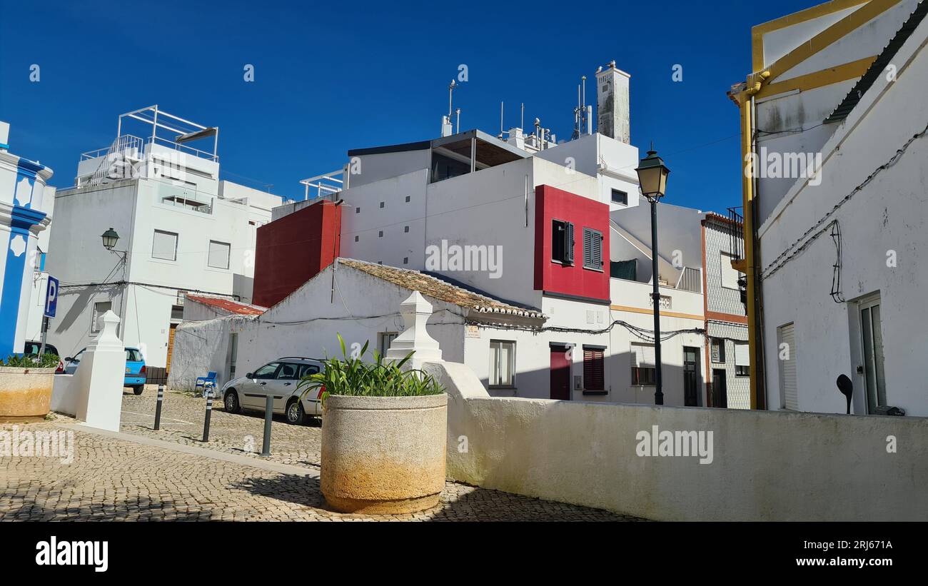 Il villaggio di Alvor, in Portogallo, con edifici d'epoca e automobili parcheggiate nelle strade acciottolate Foto Stock