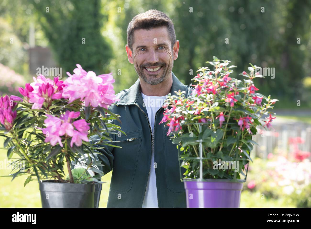 felice e attraente giardiniere maschio che lavora con fiori colorati Foto Stock