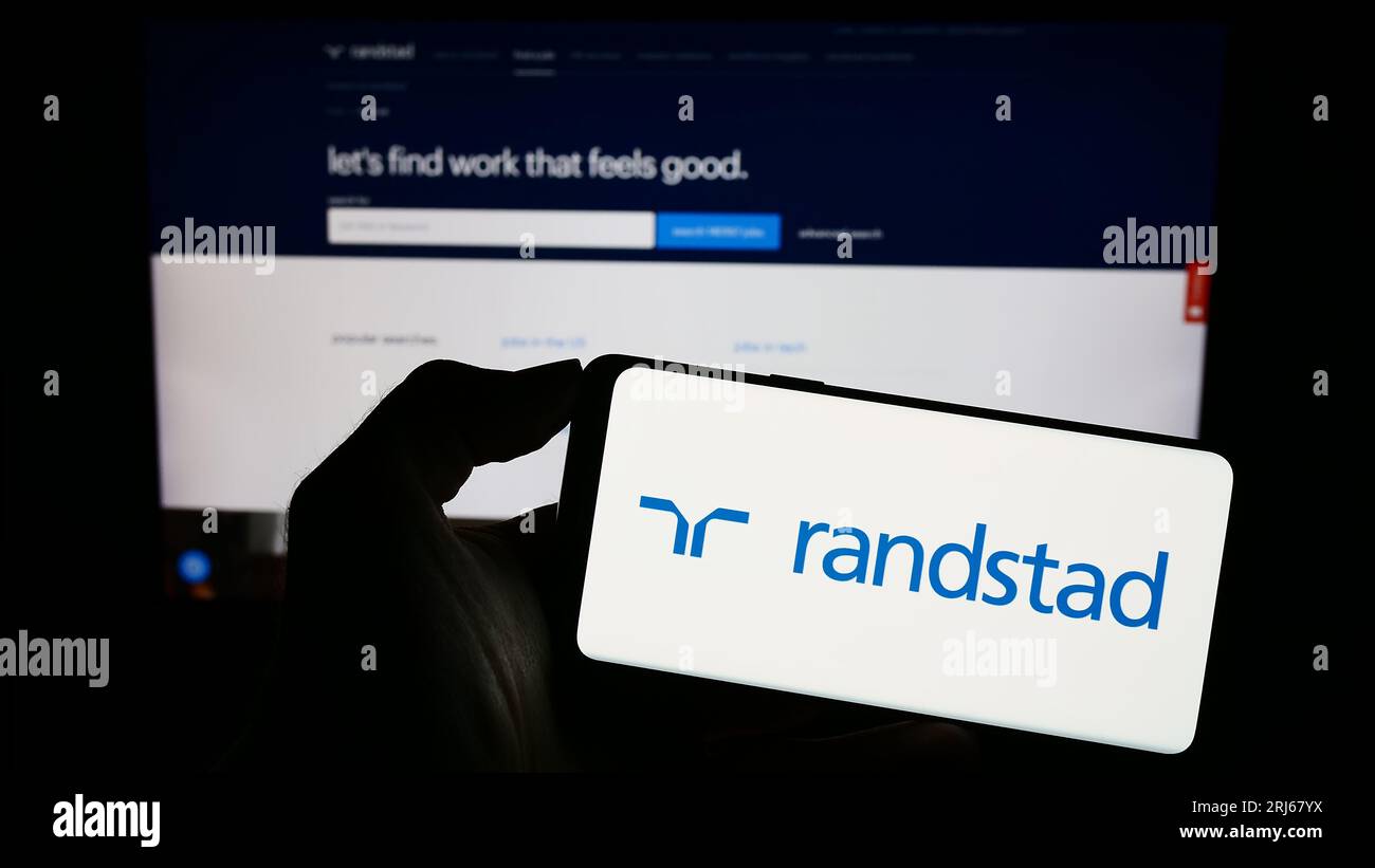Persona che possiede un telefono cellulare con il logo della società olandese delle risorse umane Randstad NV sullo schermo davanti alla pagina Web. Concentrarsi sul display del telefono. Foto Stock