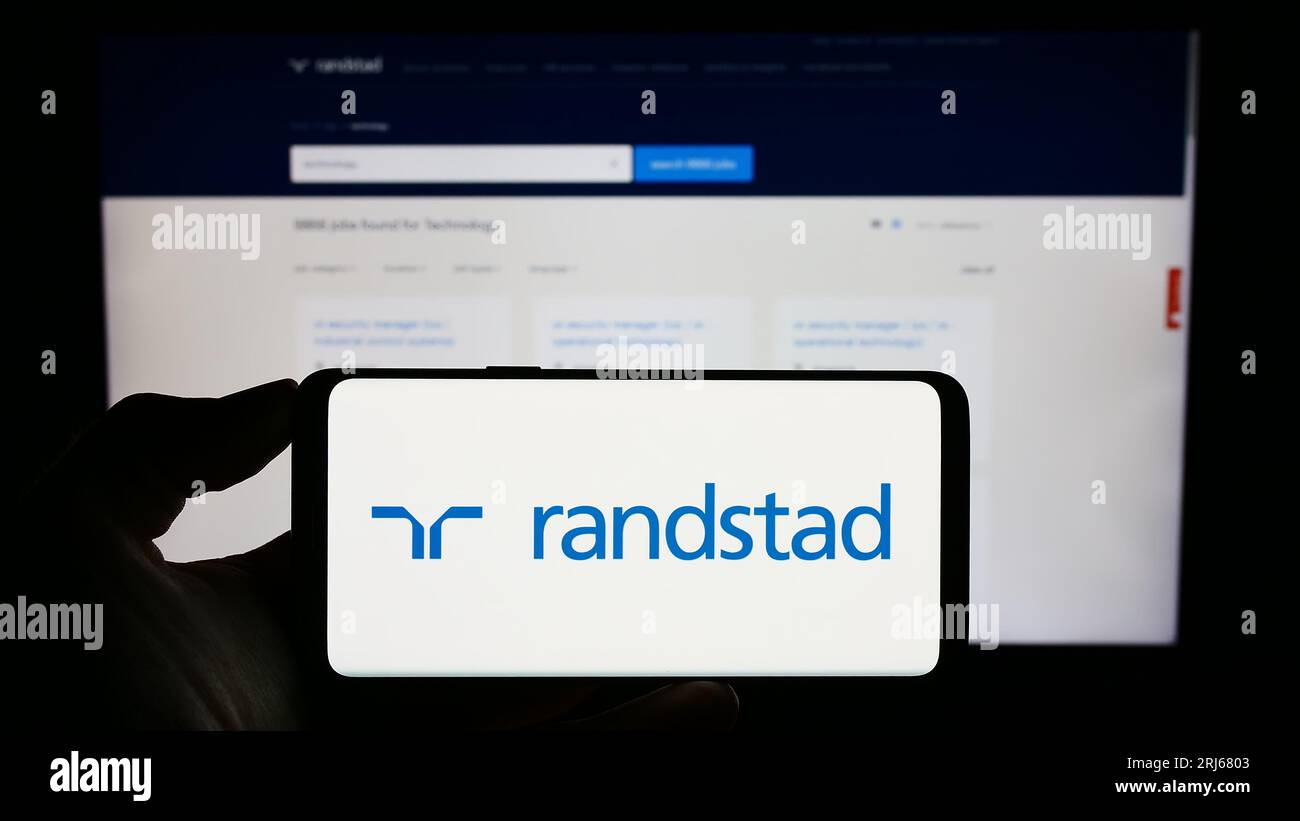Persona in possesso di un cellulare con il logo della società olandese delle risorse umane Randstad N.V. sullo schermo di fronte alla pagina Web aziendale. Concentrarsi sul display del telefono. Foto Stock