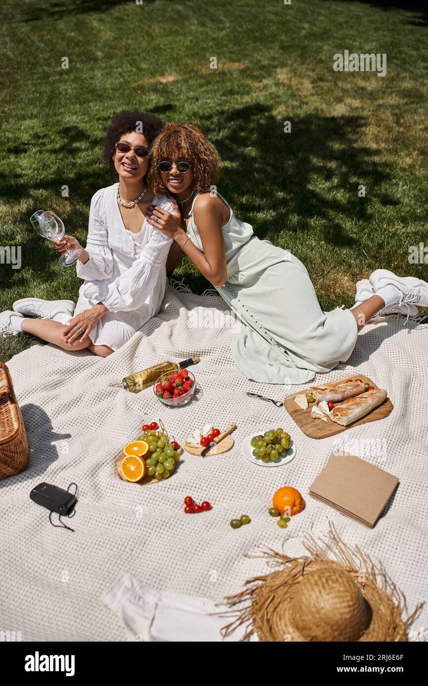picnic estivo con amiche afroamericane vicino a frutta e verdura fresche nel parco Foto Stock