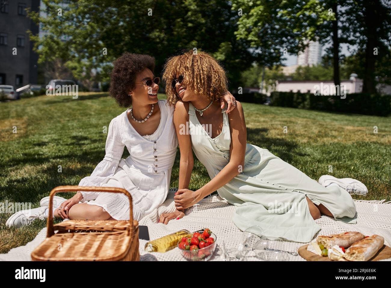 felici ragazze afroamericane che si guardano, coperta, cibo e vino, picnic estivo Foto Stock