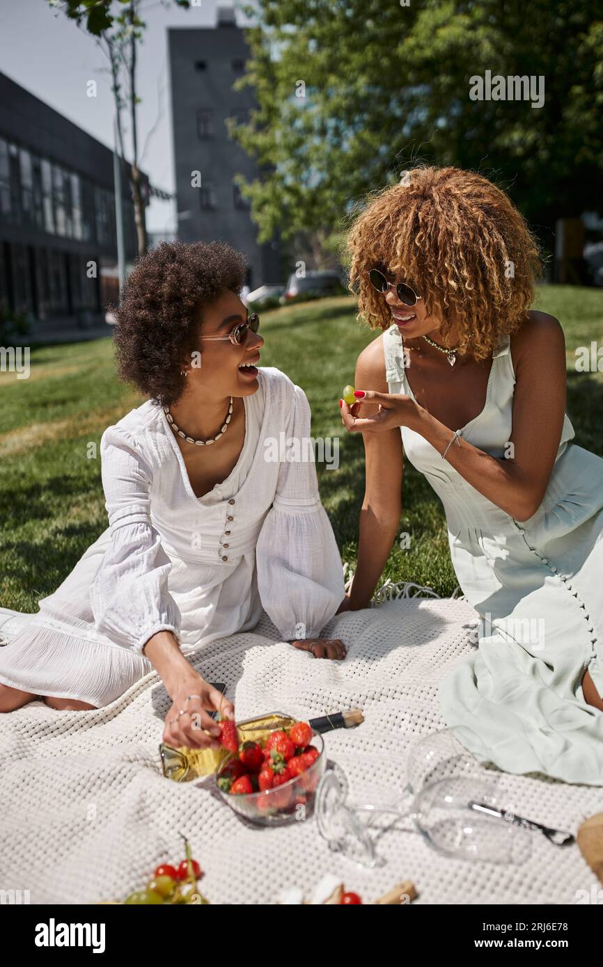 gioiose donne afroamericane che mangiano frutta e chiacchierano durante il picnic estivo nel parco Foto Stock