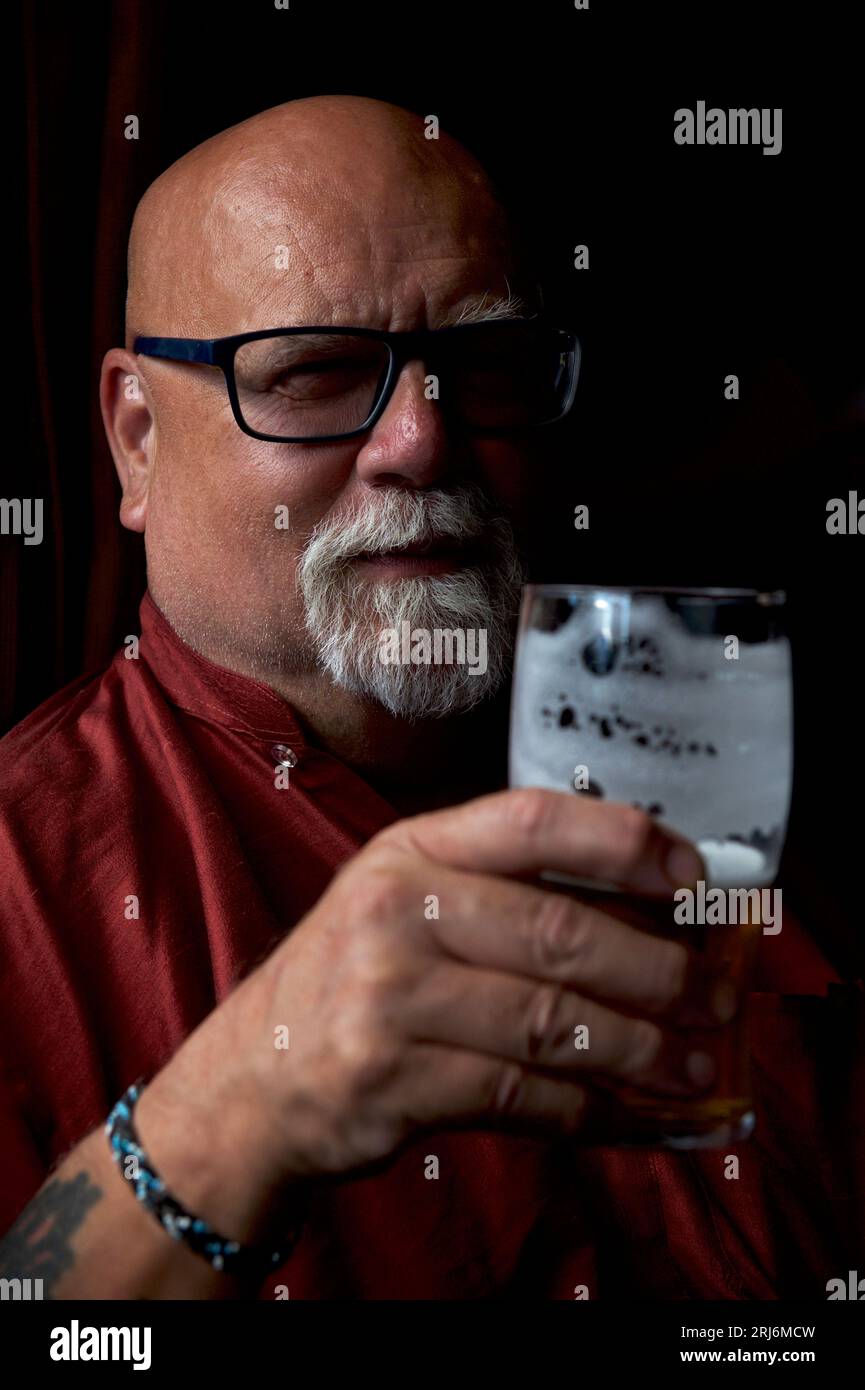 Uomo anziano con espressioni stravaganti, mentre si chiede se la sua birra og al bicchiere sia mezzo vuota o mezzo piena Foto Stock