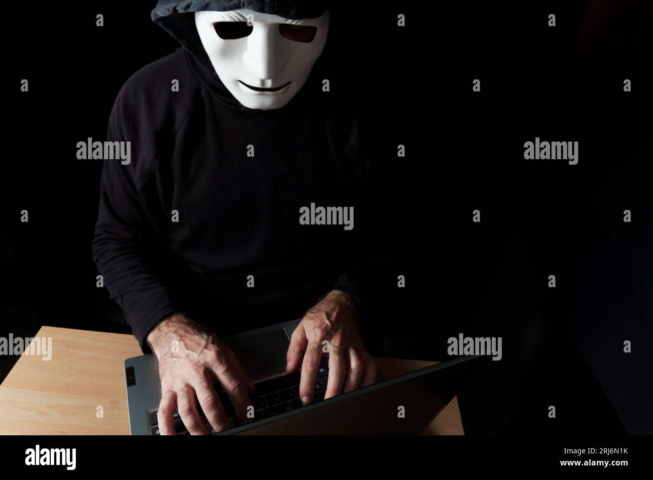 hacker vestito di nero, con cappuccio e maschera che digita su un concetto di cybercrimine Foto Stock