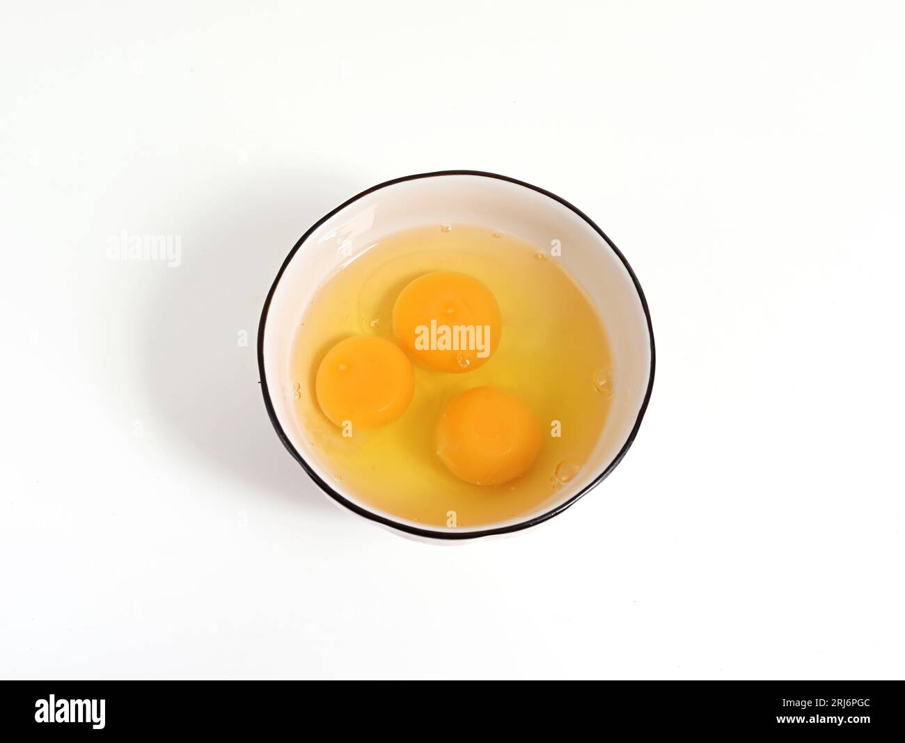 Immagine ravvicinata dei tuorli d'uovo in una ciotola su una superficie bianca e piatta Foto Stock