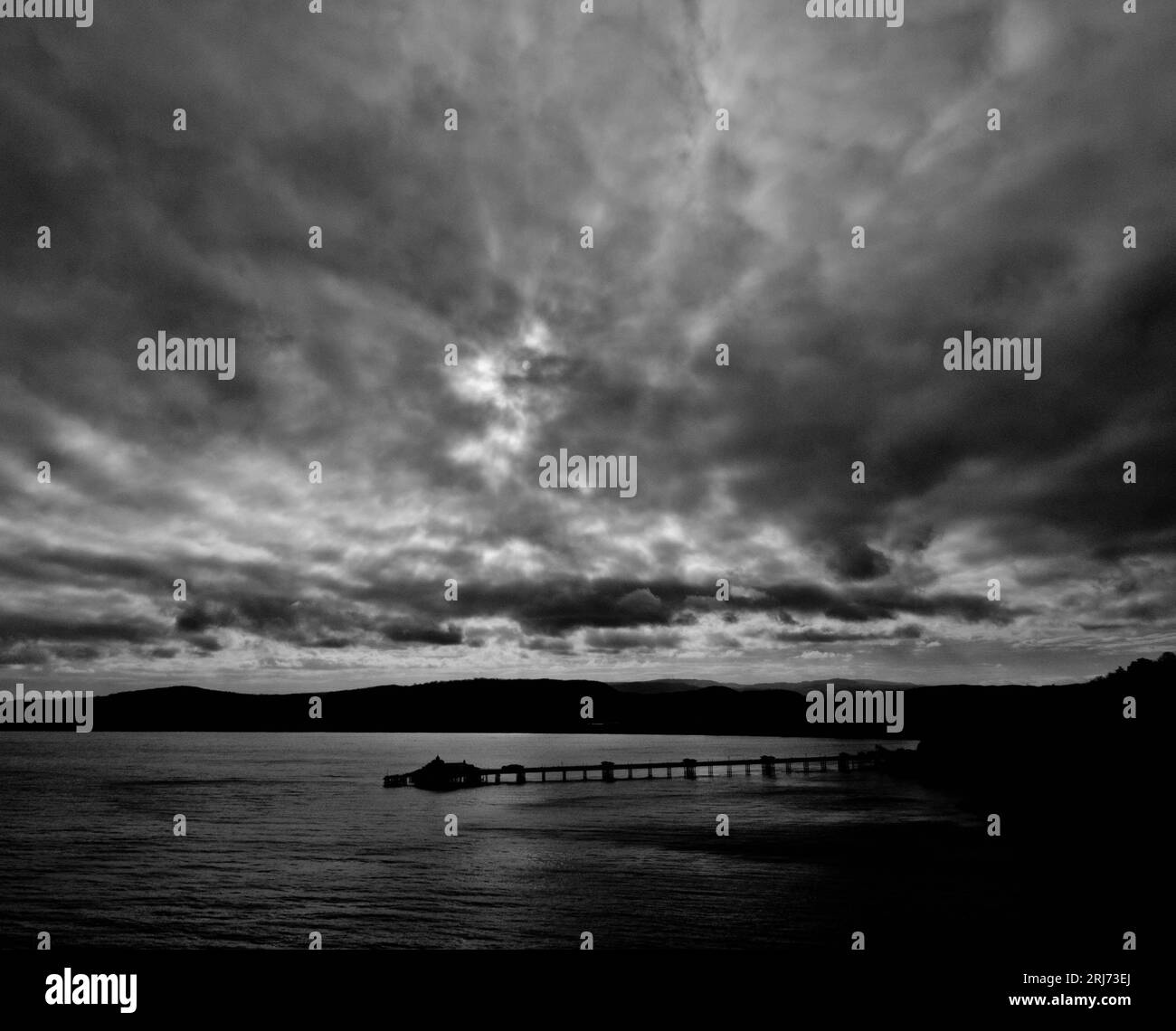 Una tranquilla scena costiera con un molo che si estende in un cielo nuvoloso sopra le acque tranquille Foto Stock