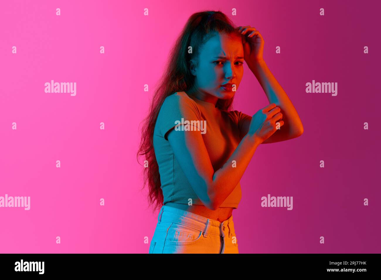 Giovane ragazza in piedi con il volto spaventato su sfondo rosa in studio con luce al neon. Sentirsi male e nervoso Foto Stock