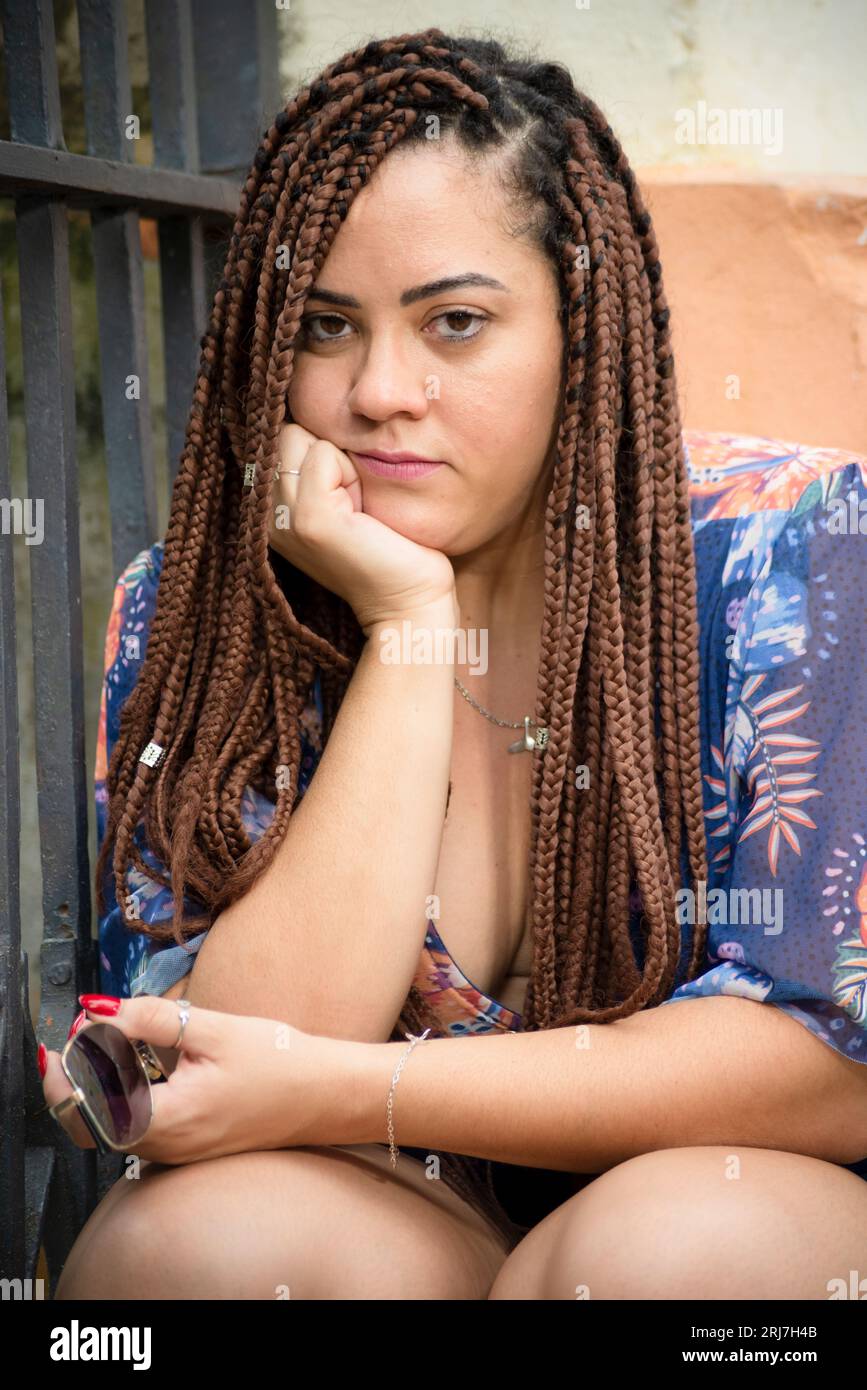 Ritratto di una bella donna con trecce nei capelli e mano sul mento che guarda la fotocamera. Pelourinho, Brasile. Foto Stock