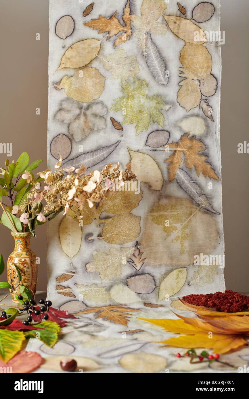 Foglie autunnali, noci, bacche e un vaso con bouquet essiccato su sfondo di strisce di tessuto tinte a mano con una tecnica di ecostampa Foto Stock