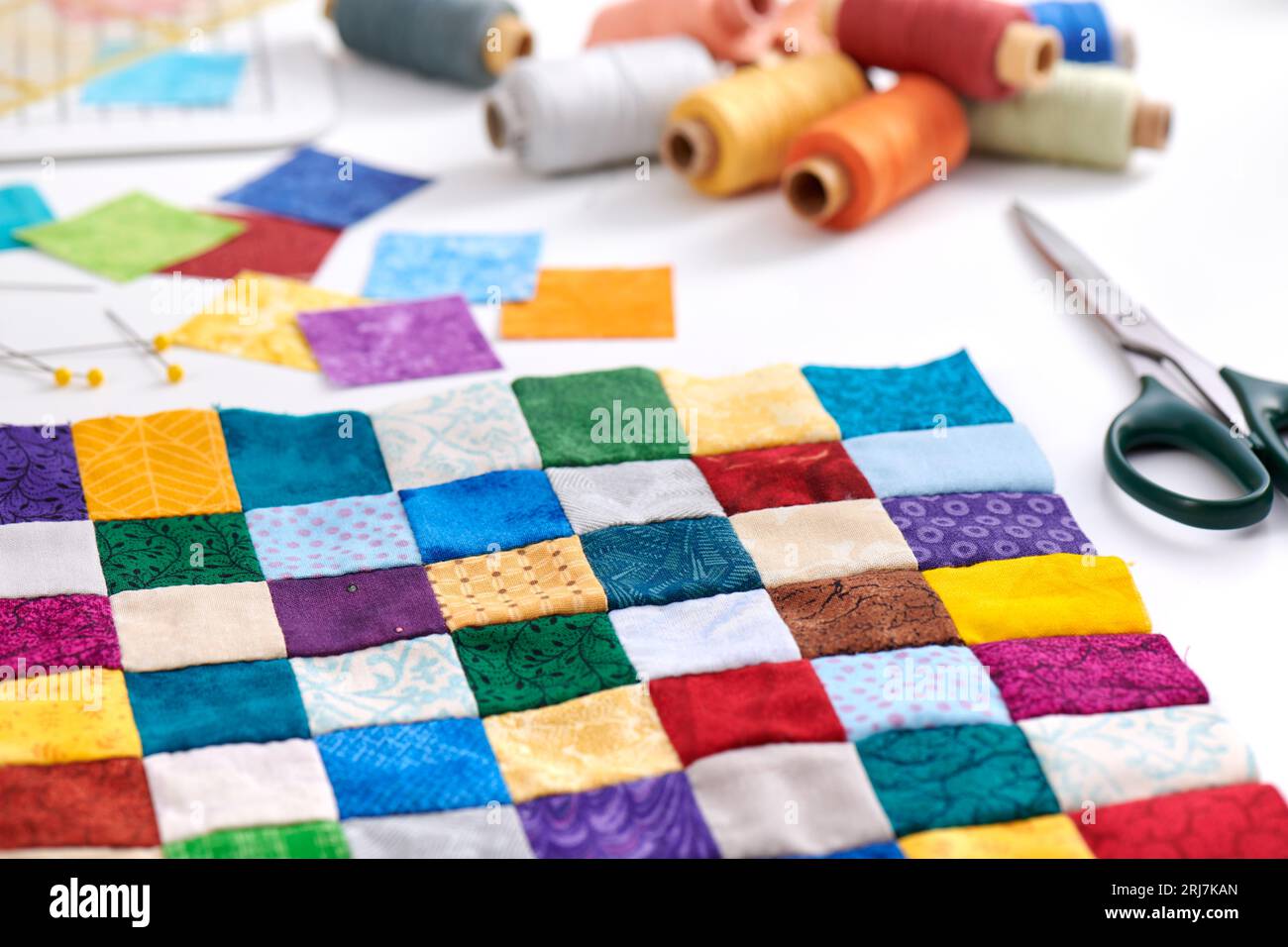 Parte colorata di trapunta cucita da pezzi quadrati, bobine di filo, forbici, accessori per trapuntatura e cucito Foto Stock