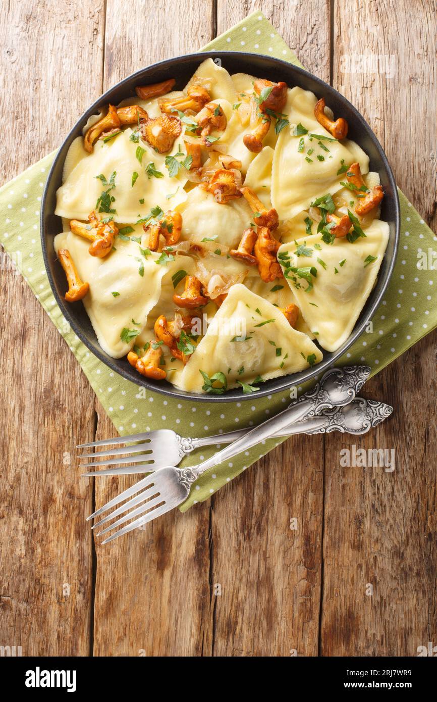Triangoli è una semplice pasta a forma di triangolo ripiena di funghi chanterelle, cipolla ed erbe sul piatto sul tavolo di legno. Verticale superiore Foto Stock