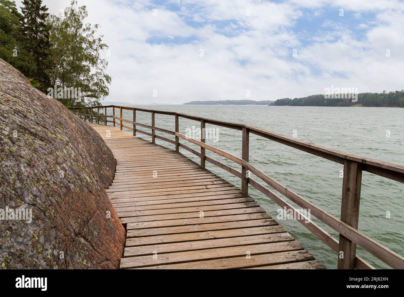 Passerella rialzata in legno sul mare tra la roccia e il Mar Baltico a Mariehamn, Isole Åland, Finlandia, in una giornata nuvolosa. Foto Stock