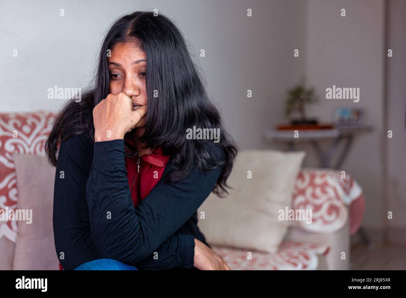 Una giovane donna con i capelli lunghi è seduta su un divano, sembra triste e disorientata Foto Stock