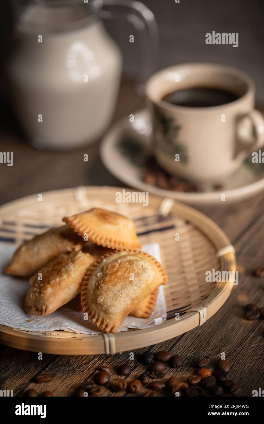 Polsini di curry fritti su un piatto di rattan con una tazza di caffè. Spuntini malesi. Colazione malese. Asian Foods. Foto Stock