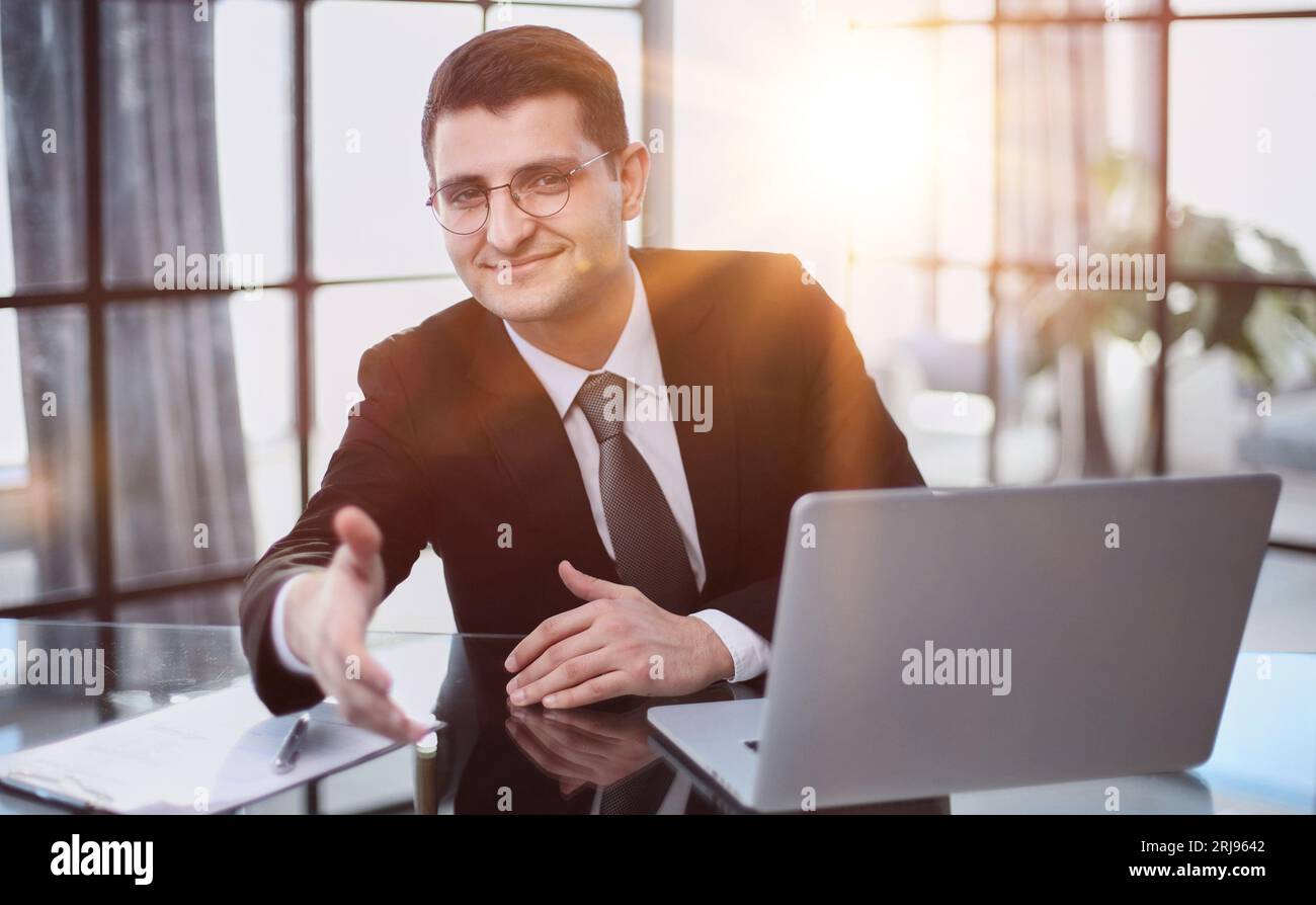 lavorare al computer, fa un gesto invitante, si offre di sedersi per un colloquio Foto Stock