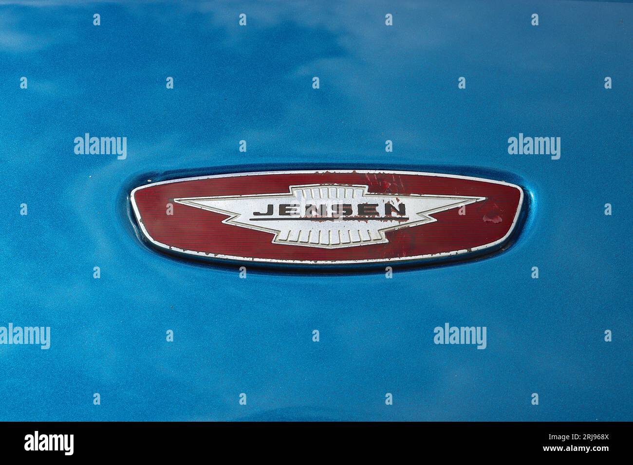 Iconico logo Jensen sul cofano che richiede il restauro di un'auto sportiva Interceptor blu metallizzato, esposta su un'auto di progetto in attesa di restauro completo. Foto Stock