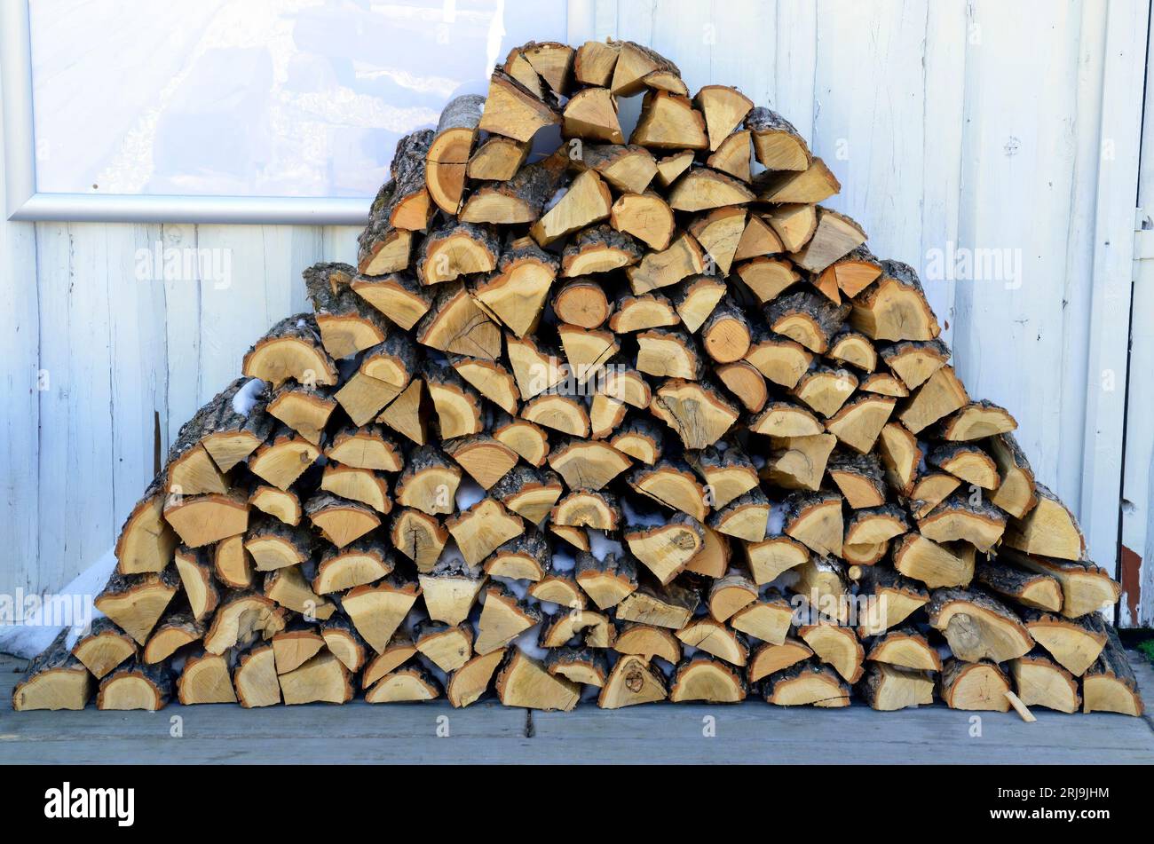 Una pila di legna da ardere ordinatamente impilata con neve su sfondo bianco Foto Stock