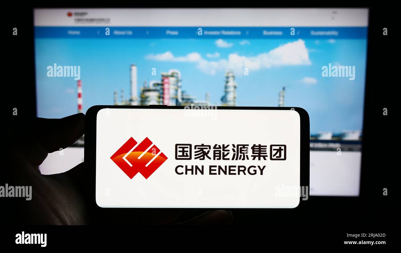 Persona che possiede il cellulare con il logo della società China Energy Investment Corporation sullo schermo di fronte alla pagina Web Bsuiness. Concentrarsi sul display del telefono. Foto Stock