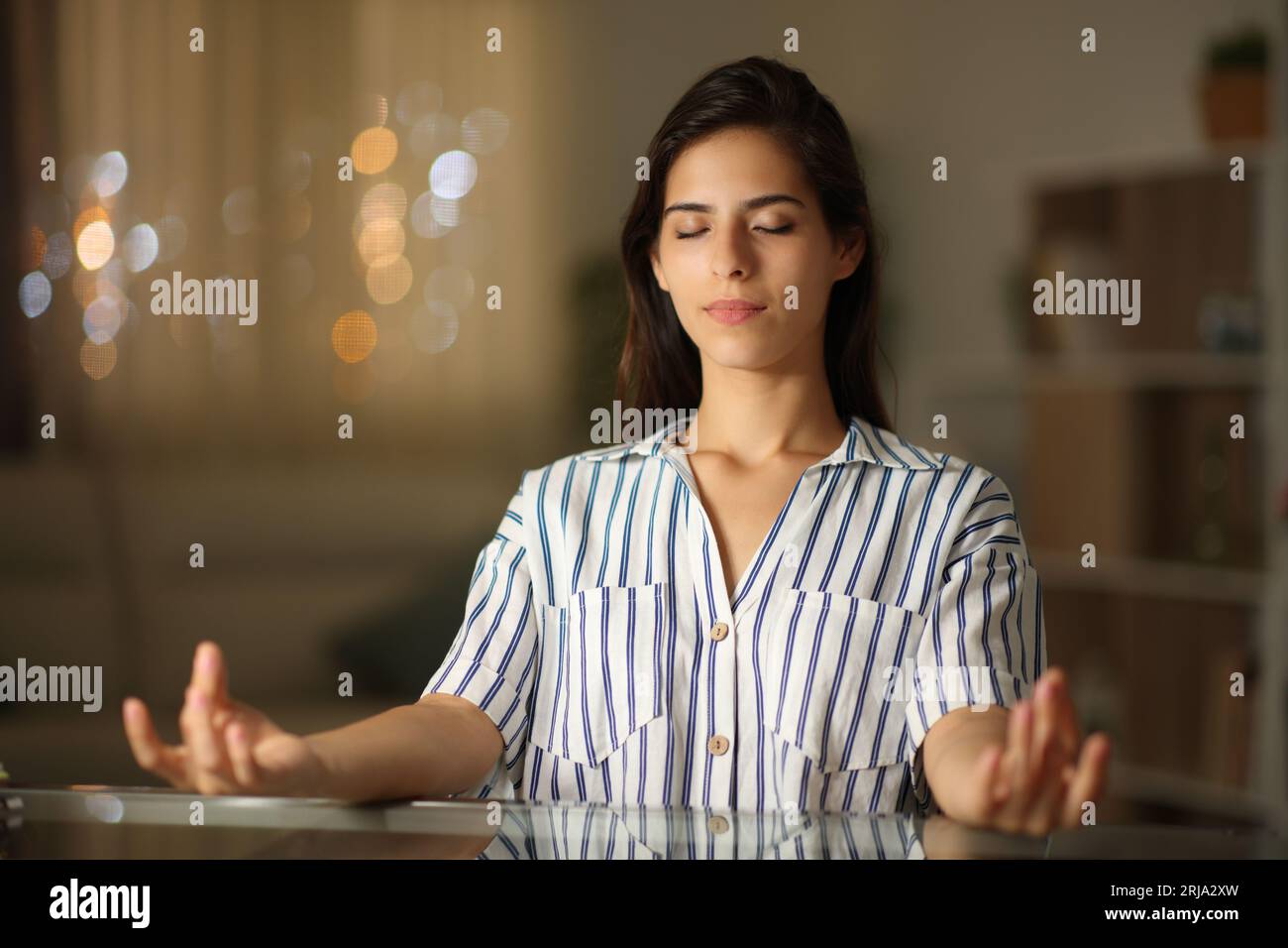 Donna che solleva lo stress facendo yoga in una scrivania la notte a casa Foto Stock
