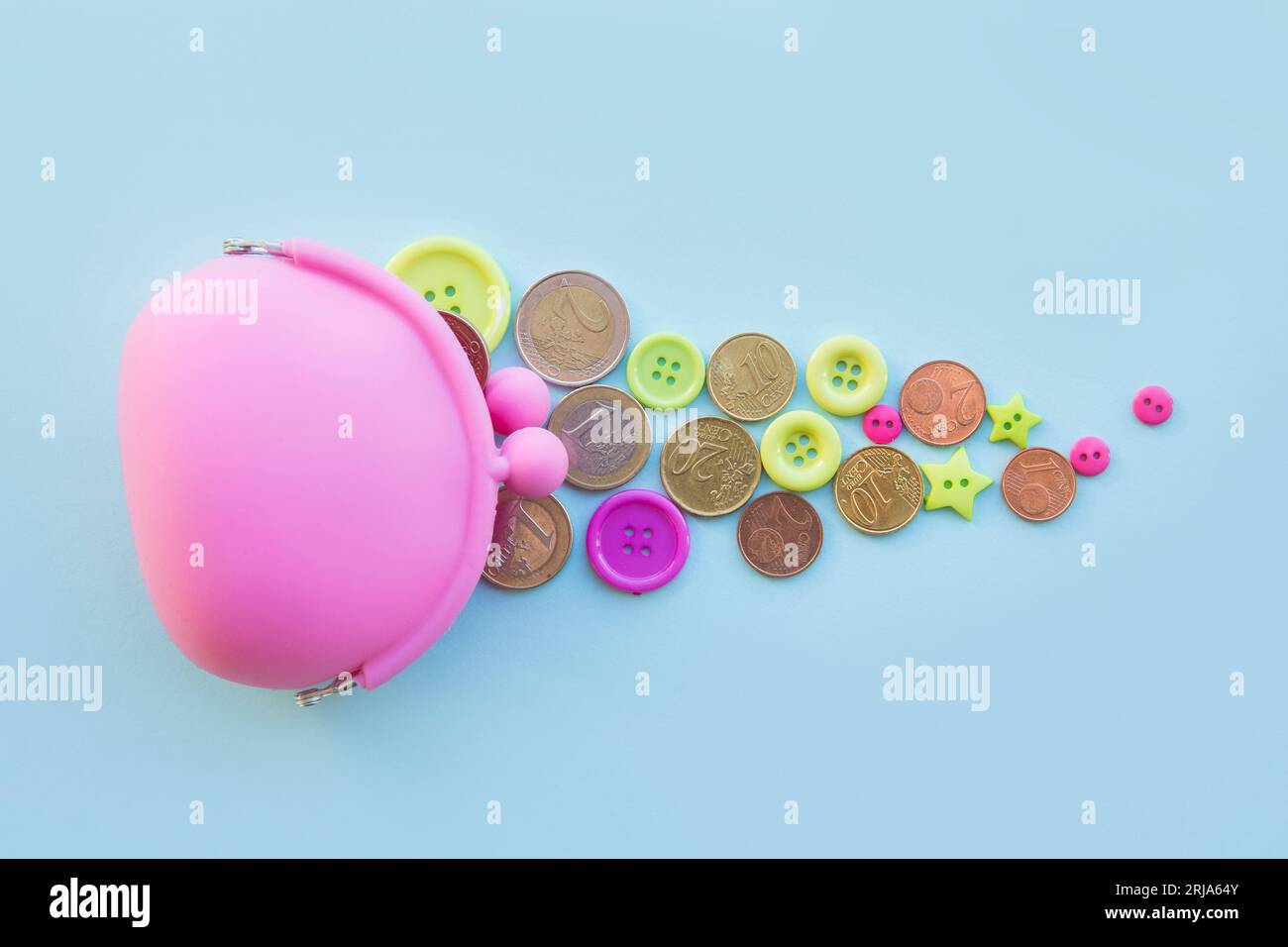 Concetto di soldi per bambini. Monete e bottoni in euro sparsi intorno al portafoglio di colore rosa su sfondo blu. Copia spazio. Foto Stock