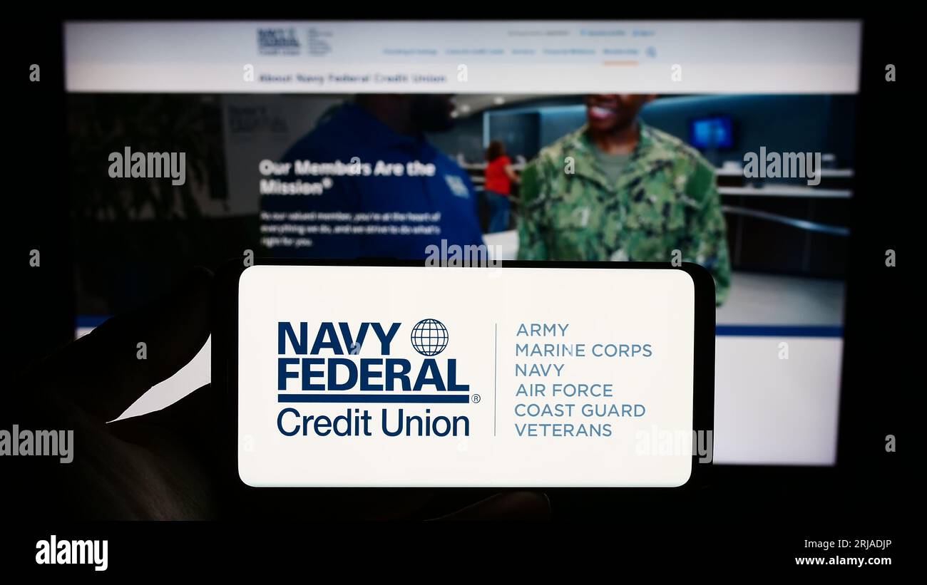 Persona che possiede uno smartphone con il logo dell'istituto finanziario Navy Federal Credit Union sullo schermo davanti al sito Web. Concentrarsi sul display del telefono. Foto Stock