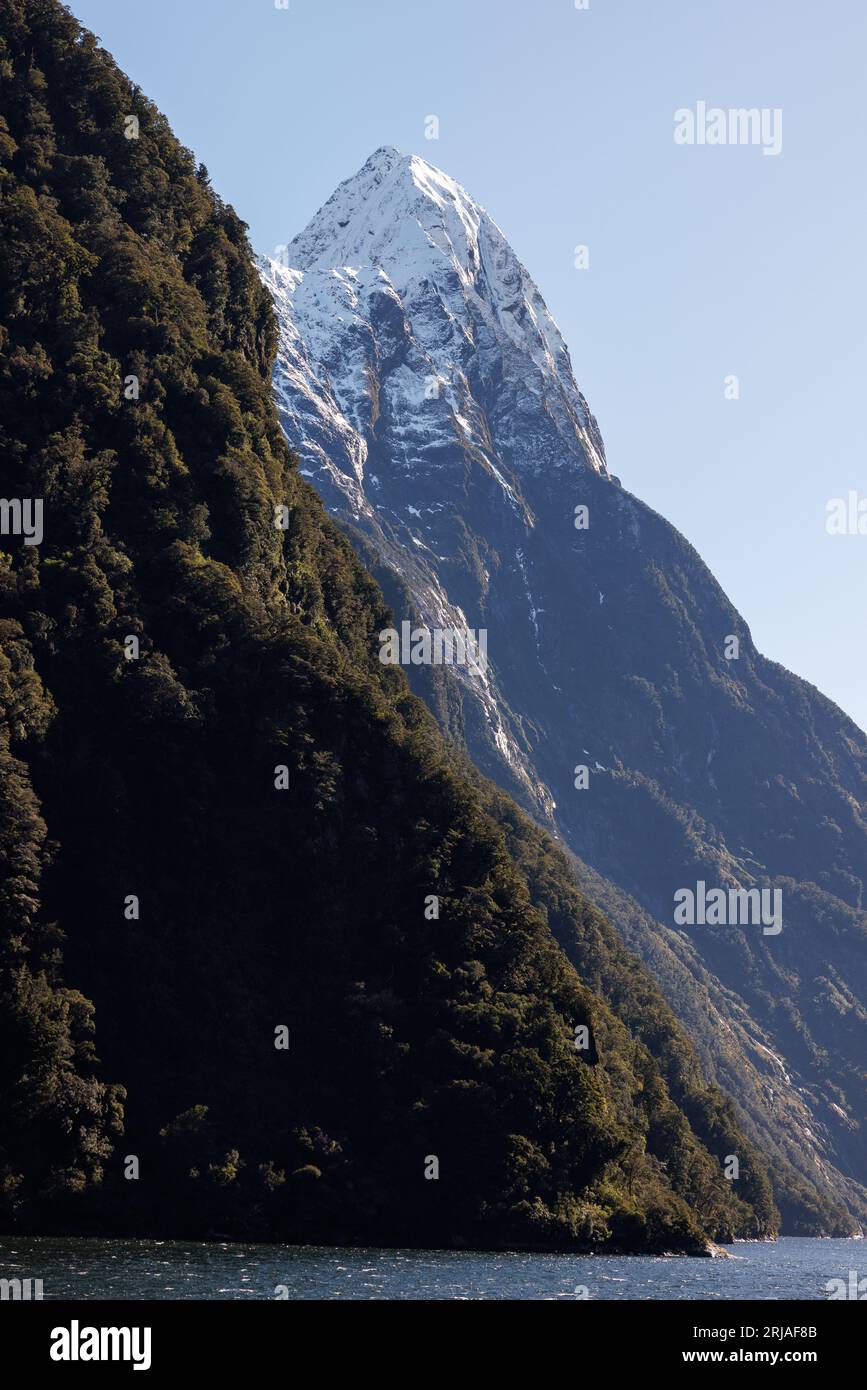 Il picco del mitro che esce da dietro un'altra collina. Mitre Peak si trova nel Milford Sound, nuova Zelanda, ed è coperto di neve Foto Stock