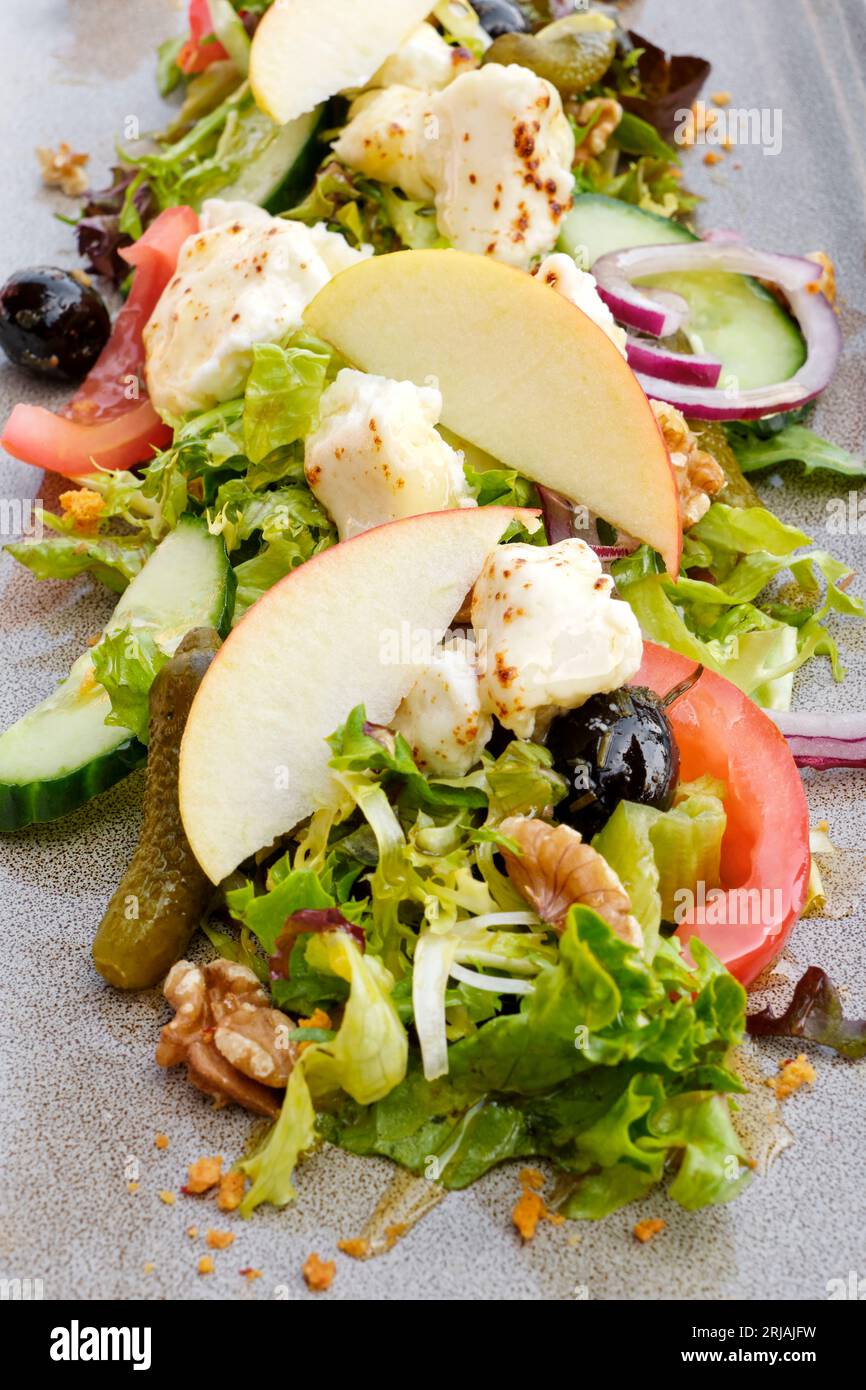 Primo piano di un'insalata fresca con formaggio di capra grigliato, mela, sedano, noci, pomodoro, cipolla rossa, lattuga, cetriolo, pinoli, noci e olive Foto Stock