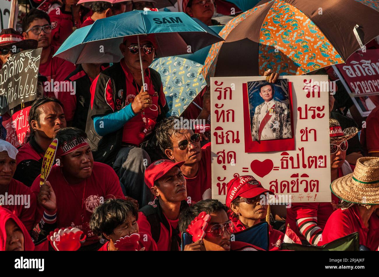 Manifestante con camicia rossa con un cartello con scritto tailandese con foto di Thaksin Shinawatra durante una protesta con camicia rossa. Phan fa Bridge, Bangkok, Thailandia. © Kraig Lieb Foto Stock