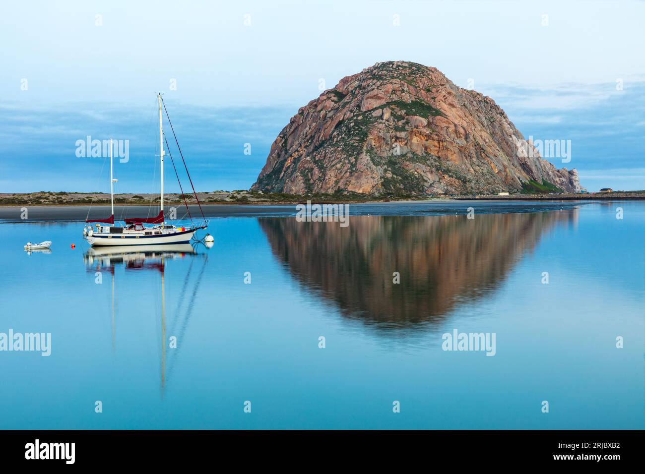 Vista mattutina di Morro Rock a Morro Bay, California. Porto in primo piano con barca a vela. Riflesso a specchio sull'acqua. Foto Stock